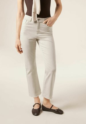 Mujer con vaqueros cortos de color beige claro y zapatos Mary Jane negros, con una mano en el bolsillo y una camiseta de tirantes oscura.