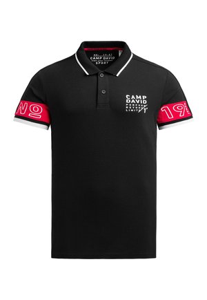 Polo de color negro con un corte ajustado, cuello blanco en contraste y detalles en rojo en las mangas que presentan texto y diseños gráficos en blanco.