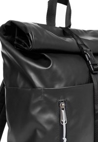 Zwarte roll-top rugzak gemaakt van gestructureerd waterproof materiaal, met een voorvak met rits en zilverkleurige hardware en verstelbare schouderbanden.