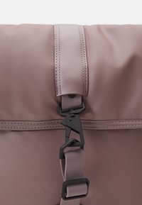 Miękki różowy plecak o eleganckim designie, z magnetycznym zapięciem i czarnym hardwarem, z kontrastowym przeszyciem na gładkiej powierzchni materiału.