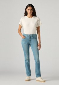 Vaqueros de un azul claro con un corte ajustado, combinados con una camiseta de manga corta color crema. Los vaqueros cuentan con cinco bolsillos y un cierre de botones.