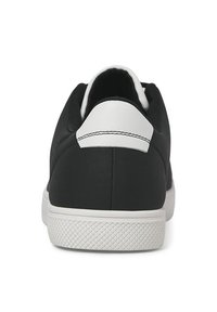 Sort sneaker med en hvid hælflap, gummisål og glat tekstur. Bagfra fremhæves syningerne og det minimalistiske design.