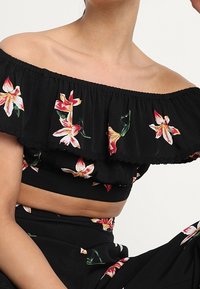 Svart off-shoulder crop top med blommigt broderi i rött och vitt. Har en flerlagers ruffle-design och texturerad tyg.