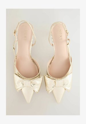 Złote metaliczne obcasy slingback z ostrym nosem i dużą kokardą z przodu. Teksturowana powierzchnia z gładkim wnętrzem.