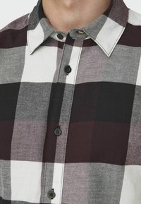 Camisa de cuadros con cuadrados en negro, blanco y burdeos, con cuello abotonado y cierres de botones, hecha de una mezcla de algodón texturizado.