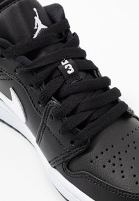 Baskets en cuir noir avec dessus texturé, logo blanc, lacets noirs et détails perforés. Semelle en caoutchouc avec accent blanc.