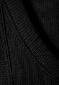 Tissu en tricot noir avec une texture côtelée et un design en col en V, présentant des coutures soignées le long des bords.