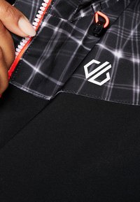 Schwarze Sportjacke mit geometrischem Muster, rotem Reißverschluss und einem weißen Logo auf der unteren rechten Seite. Glatte Textur und taillierte Passform.