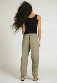 Lätta khakifärgade byxor med en avslappnad passform och elastisk midja, med en subtil blommig design på vänster ben. Kombineras med en svart linne.