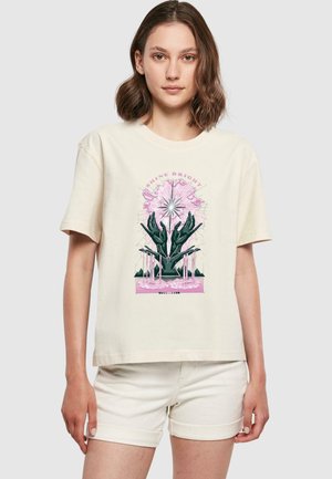 T-shirt beige à manches courtes avec un design graphique coloré de mains et d'éléments floraux avec le texte "SHINE BRIGHT". Matière en coton doux.