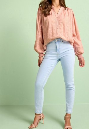 Pink long-sleeve blouse with textured pattern, buttoned front, and elastic cuffs paired with light blue fitted jeans and nude heeled sandals.
