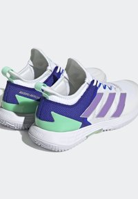 Białe buty sportowe z fioletowymi i zielonymi akcentami, siateczkowa cholewka, trzy fioletowe paski, lekka podeszwa oraz teksturowany zielony detal na pięcie.