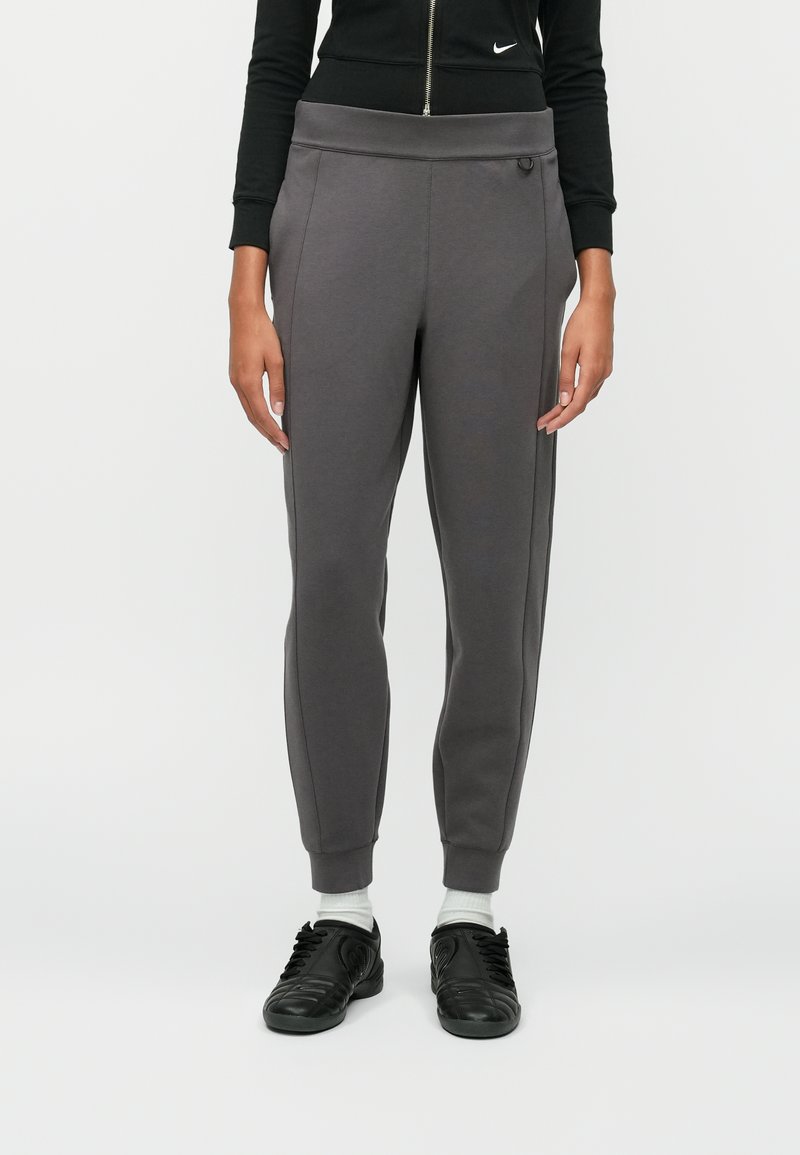 Pantalons de survêtement gris avec un design fuselé, taille élastique et rayures sur les côtés. Présente un tissu texturé et un logo discret sur la taille.