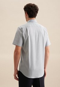 Camicetta a maniche corte di un azzurro chiaro, realizzata in tessuto morbido, con colletto classico e orlo curvo. Presenta dettagli di cuciture sottili.