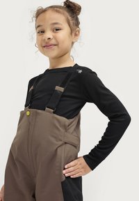 Zwarte lange mouwen shirt met een klein geborduurd detail, gecombineerd met bruine waterdichte overall met verstelbare schouderbanden en zijzakken.