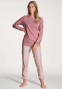 Long-sleeve pink top paired with patterned pajama pants featuring purple cuff accents and intricate geometric designs in pastel colors.
