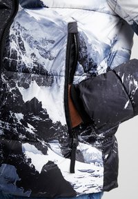 Prošívaná bunda s černobílým potiskem hor, hladkou látkou, kapsou na zip a elastickými manžetami pro teplo a pohodlí.