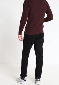 Pull côtelé bordeaux, pantalon noir et baskets blanches. Le pull présente un motif texturé et le pantalon a une coupe droite.