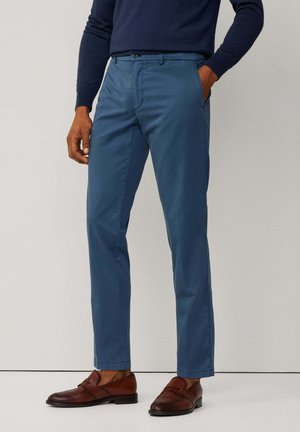 Chinos en coton bleu à jambes droites, avec fermeture à bouton et poches latérales, associés à des mocassins en cuir marron.