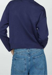 Suéter de punto azul marino con un diseño recortado y un ajuste holgado, combinado con jeans de mezclilla de cintura alta en azul claro que tienen bolsillos traseros.
