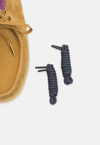Tan suede shoe with a purple accent, featuring gold hardware and two rolled navy shoelaces with plastic aglets.
