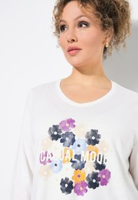 Weißes V-Ausschnitt-T-Shirt mit floralem Druck in Lila, Schwarz, Blau und Gelb, mit dem Text "CASUAL MOOD" in fetten Buchstaben.