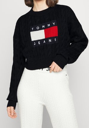 Pull court noir en maille torsadée avec le logo Tommy Jeans en blanc et rouge, assorti à un pantalon blanc en maille torsadée.