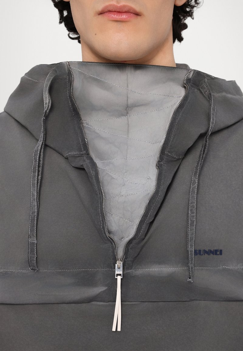 Felpa grigia con zip, caratterizzata da un interno foderato, coulisse sul cappuccio e un piccolo logo sul davanti. Tessuto testurizzato con una finitura liscia.