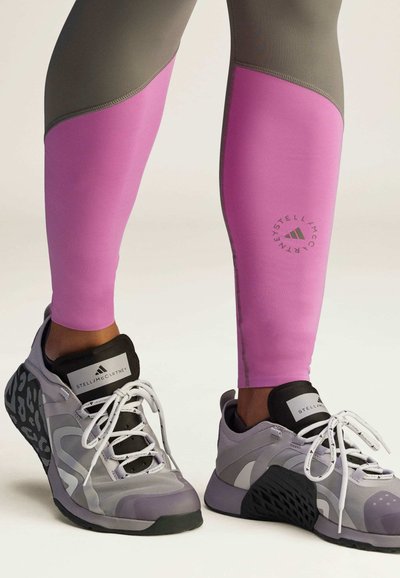 Leggings de material rosa y gris con una textura suave. Zapatillas en gris claro y negro con una suela estampada y cordones visibles.