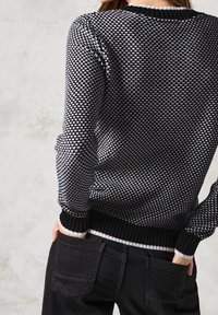 Czarnobiały sweter dzianinowy z długimi rękawami, prążkowanym dekoltem i ściągaczami, połączony z czarnymi spodniami z tylnymi kieszeniami.