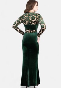 Grünes Samtkleid mit langen Spitzensäulen und floralem Stickereimuster. Figurbetonter Oberteil, ausgestellter Saum und glatte Textur.