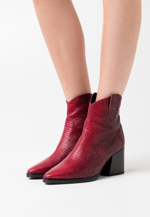 Bottines rouges en matériau synthétique texturé, avec un bout pointu, un talon block et une coupe de style western avec des accents de couture sur les côtés.