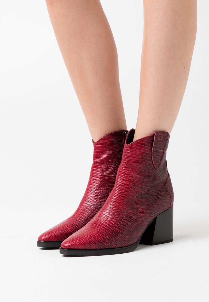 Bottines rouges en matériau synthétique texturé, avec un bout pointu, un talon block et une coupe de style western avec des accents de couture sur les côtés.
