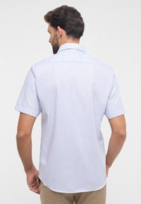 Camicia azzurra a maniche corte con un motivo testurizzato, colletto classico e taglio dritto, indossata con pantaloni color khaki.