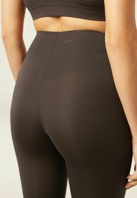 Leggings marron taille haute en tissu extensible, dotés d'une texture lisse et d'une discrète marque sur la taille, conçus pour le confort.
