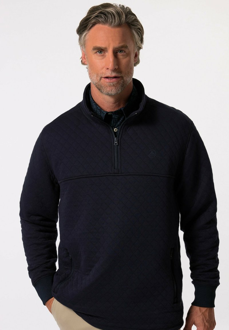 Sudadera acolchada navy con cuello con cremallera, patrón texturizado de diamantes y bolsillos laterales. Presenta puños y dobladillo de canalé.