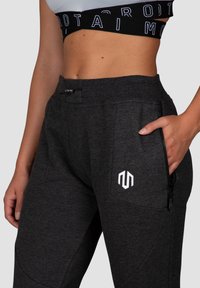 Dark gray jogger pants with a ribbed waistband, zipper pocket, and a logo on the side; smooth texture and tapered design.