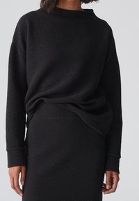 Pull noir texturé à manches longues et col rond, accompagné d'une jupe taille haute assortie, présentant un look harmonieux.