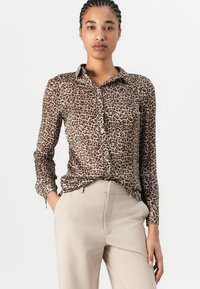 Langermet bluse med leopardmønster laget av lett stoff, med krage og knappelukking. Kombinert med beige bukser.