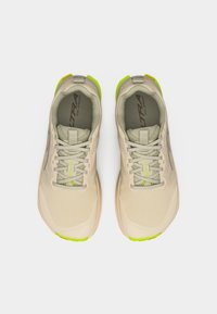 Ζευγάρι μπεζ παπούτσια για τρέξιμο σε μονοπάτια με ανοιχτοπράσινες λεπτομέρειες, δεμένα και φαίνονται από πάνω σε λευκό φόντο.