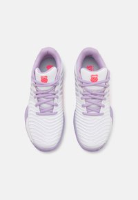 Tênis brancos de atletismo com detalhes em roxo, parte superior texturizada e sistema de atilhos tradicional. Apresenta um logo na lingueta e um colar acolchoado.