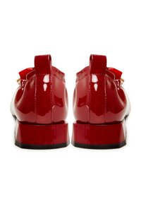 Zapatos de charol rojos con acabado brillante, con un tacón bajo, forma redondeada y un detalle en bucle en la parte trasera.