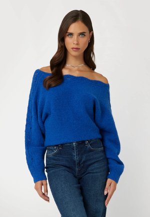 Maglione lavorato a maglia blu senza spalle, con maniche lunghe, tessuto strutturato e dettagli a costine, abbinato a jeans blu a vita alta.