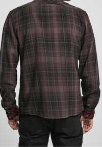 Chemise en flanelle écossaise pour homme, en marron foncé et noir avec des accents rouges, dotée d'un col et de poignets boutonnés, d'une texture lisse et d'un ourlet arrondi.