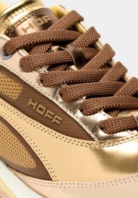 Zapatilla con diseño metálico en dorado y rosa claro, detalles en malla marrón, cordones gruesos marrones y un logo de marca en el lateral.