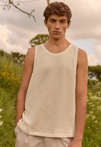 Let ca. lys, cremelavet tank top uden ærmer med et tekstureret, åbent strikket design. Har en klassisk rund hals og subtile sideslidser.