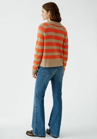 Gestreifter Pullover in Orange- und Beigetönen, mit geripptem Saum und langen Ärmeln, kombiniert mit weit geschnittenen blauen Jeans und dunklen Schuhen.