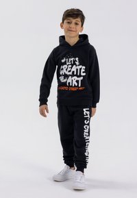 Black hoodie and sweatpants set featuring white and orange text, ribbed cuffs, and a relaxed fit. The hoodie has a drawstring and front pocket.
