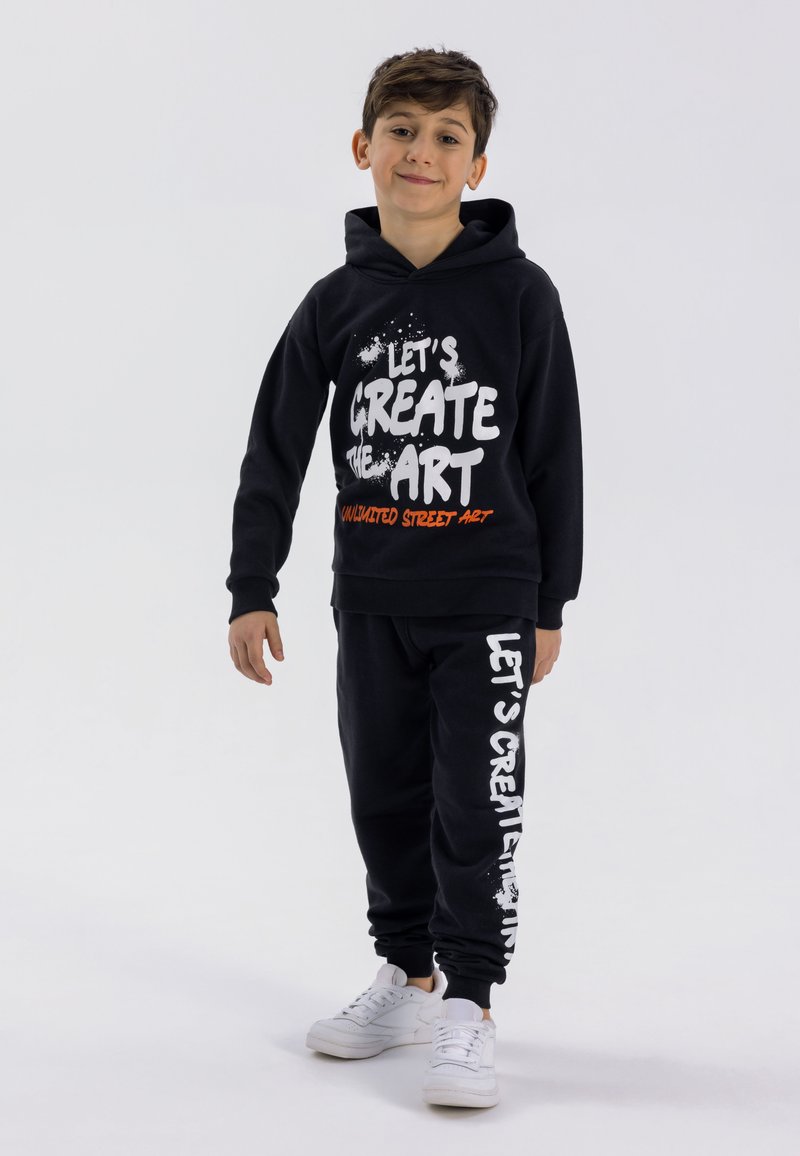 Black hoodie and sweatpants set featuring white and orange text, ribbed cuffs, and a relaxed fit. The hoodie has a drawstring and front pocket.