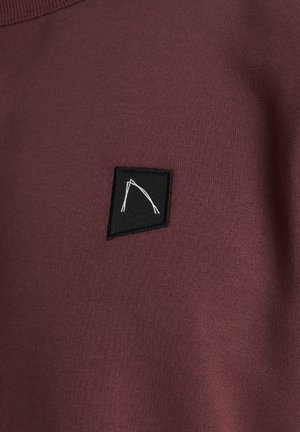 Burgundska dukserica s crnim trokutastim platnenim aplikatorom s bijelim linijskim dizajnom, ističući teksturirani pamuk.